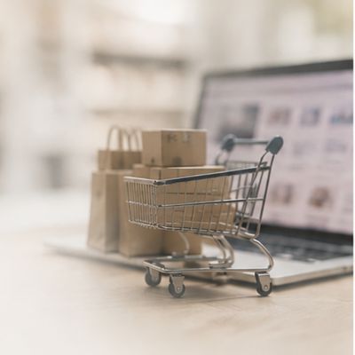 Shopping trolley with packaged goods beside an online retail screen.