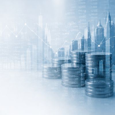 Stacks of coins with financial data and market charts in the background.